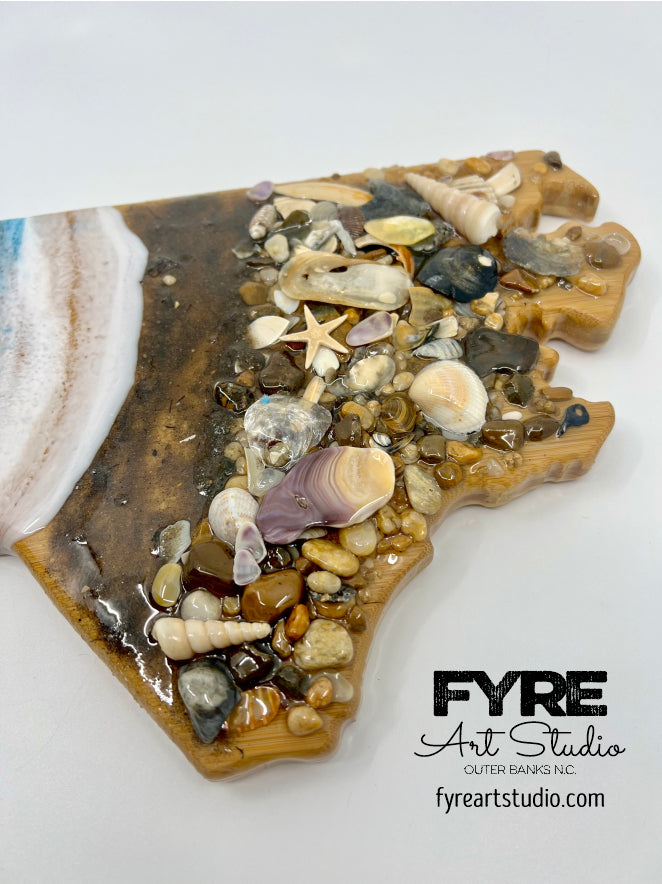 Discover the beauty and art of North Carolina State with our Ocean Resin Waves and Shells Wall Art. Hand-crafted by Fyre Art Studio in Kill Devil Hills, this 18" x 8" masterpiece captures the essence of the state's stunning coast. With the use of bamboo, Outer Banks sand, and sea shells, our resin designs are truly one-of-a-kind.Get your unique piece of OBX Ocean Decor today at fyreartstudio.com