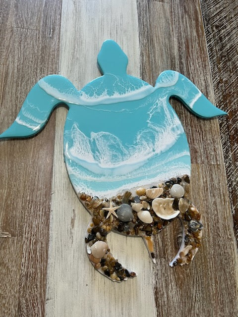 Light Blue Resin Waves Sea Turtle Wall Art with Real Outer Banks Shells on PVC sea turtle cut out. Real Outer Banks Shells. Size is 16" x 16" Take your love for the ocean to new, stylish depths with this unique Light Blue Resin Waves Sea Turtle Wall Art. Featuring real Outer Banks shells on a PVC sea turtle cut out, this piece adds a touch of quirky charm to any space. Measuring at 16" x 16", it's the perfect size to make a statement and bring a splash of the sea to your home.