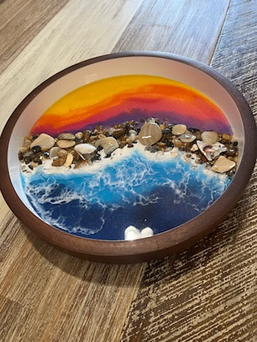 Size: 10" Round Wooden Serving Tray / Bowl  Dark wooden serving tray with white inside. Beautifully decorated with a colorful purple, orange and yellow resin sunset on the top half. Bottom half has deep blue resin ocean waves crashing onto real sea shells and polished stones collected from the beaches of the Outer Banks North Carolina.  Fyre Art Studio Outer Banks Resin Artist.