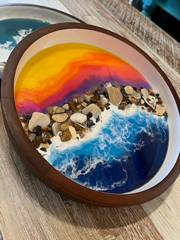 Size: 10" Round Wooden Serving Tray / Bowl  Dark wooden serving tray with white inside. Beautifully decorated with a colorful purple, orange and yellow resin sunset on the top half. Bottom half has deep blue resin ocean waves crashing onto real sea shells and polished stones collected from the beaches of the Outer Banks North Carolina.  Fyre Art Studio Outer Banks Resin Artist.