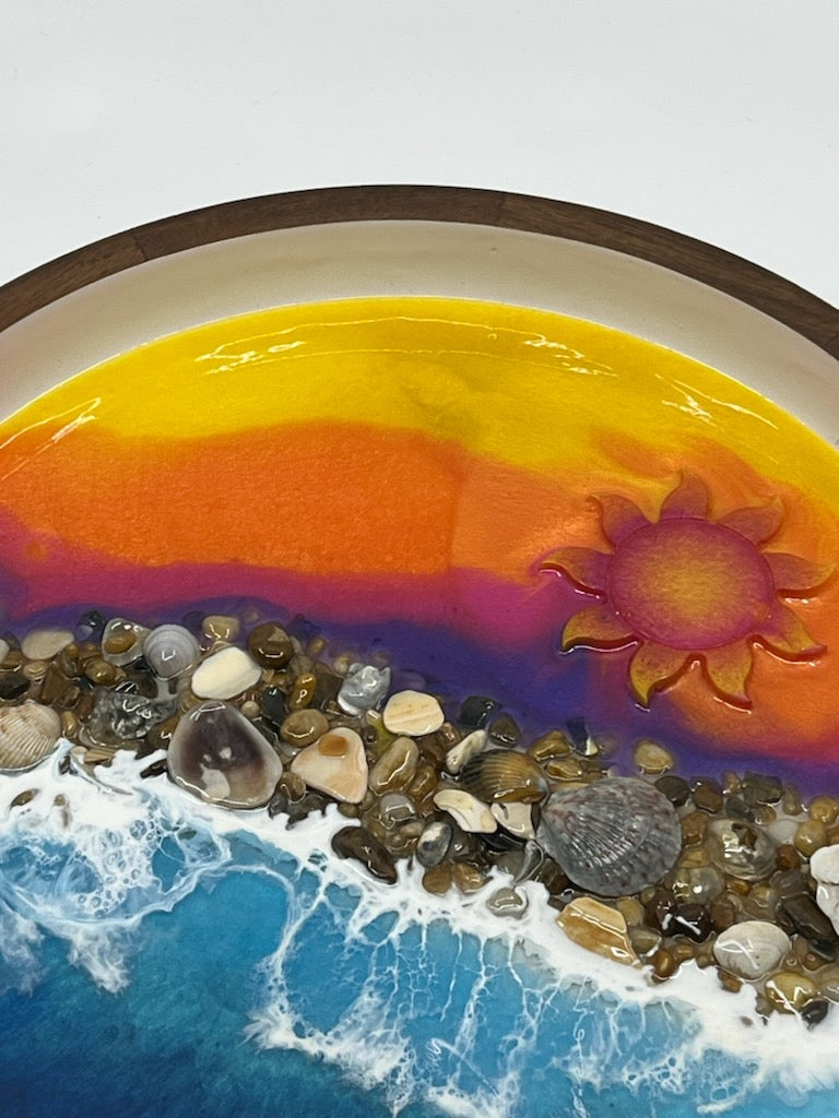 Beautifully hand crafted serving tray. Top half is a sunrise with purples, orange and yellow resin fade with a cute resin Sun. Bottom half is blue ocean waves crashing onto real Outer Banks Sea Shells in the middle. This decorative serving tray is 12" Round Dark Wood with white inside. Memorialize your last visit to the OBX with this one of a kind resin art by Fyre Art Studio in Kill Devil Hills N.C. Outer Banks Resin Artist.
