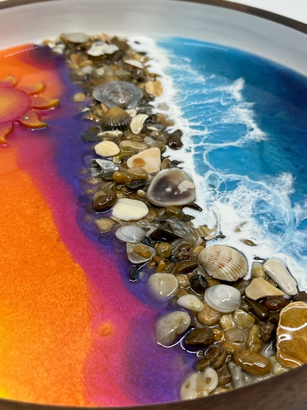 Beautifully hand crafted serving tray. Top half is a sunrise with purples, orange and yellow resin fade with a cute resin Sun. Bottom half is blue ocean waves crashing onto real Outer Banks Sea Shells in the middle. This decorative serving tray is 12" Round Dark Wood with white inside. Memorialize your last visit to the OBX with this one of a kind resin art by Fyre Art Studio in Kill Devil Hills N.C. Outer Banks Resin Artist.